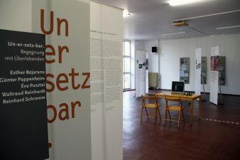 Farbfoto, links zwei bedruckte Banner mit Schriftzug Un-er-setz-bar, rechts Blick in einen Raum mit weiteren bedruckten Bannern und Tisch, auf dem ein Monitor steht