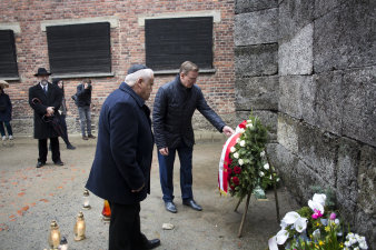 zwei Männer stehen vor einer Wand, an der Blumenkränze und Kerzen niedergelegt wurden