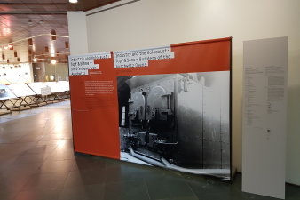 Titelwand einer Ausstellung mit Schrift und einer schwarz-weiß Fotografie eines Verbrennungsofen