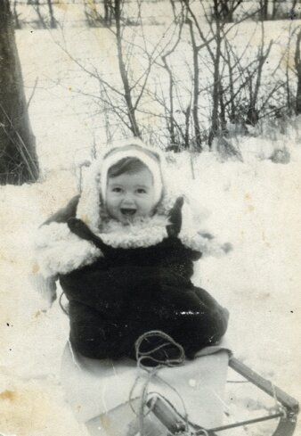 Historische Schwarz-Weiß-Fotografie von einem Kleinkind auf einem Schlitten sitzend.