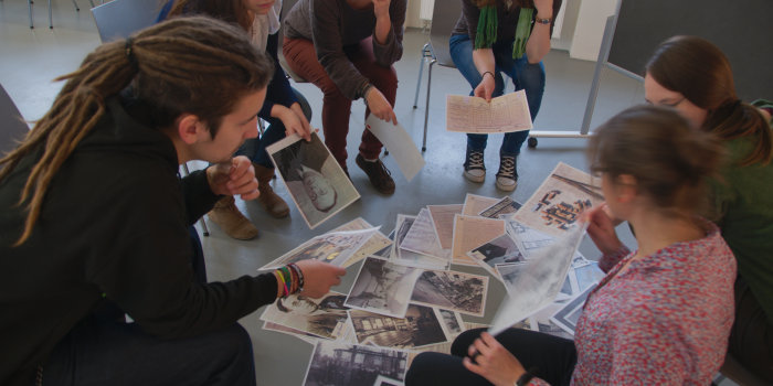 Gruppe von fünf Personen im Stuhlkreis mit mehreren Fotos auf dem Boden in der Mitte