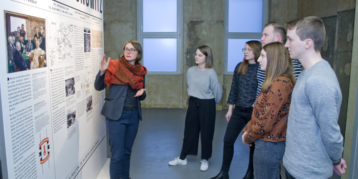Foto: Eine Besuchergruppe in der Ausstellung „Die I.G. Farben und das KZ Buna-Monowitz“ © Stadtverwaltung Erfurt/ D. Urban Eine Frau erkärt jungen Leuten etwas an einer Ausstellungstafel