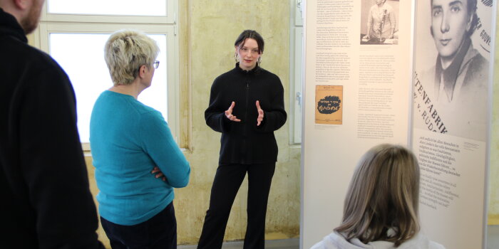 Drei Personen in einer Ausstellung und eine Person erklärt was