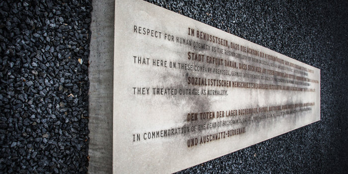 Zu sehen ist ein rechteckiger Stein mit eingravierter Schrift auf schwarzem Kies. 