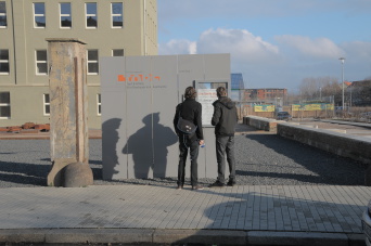 Zwei Knaben mit Mikrofon stehen vor einer Stele mit Plakat.