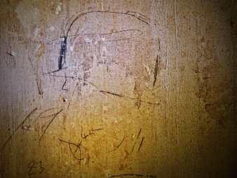 Grobe Bleistiftskizze eines Kopfes mit Helm auf gelber Wand, daneben und darunter nicht zu lesende Handschrift sowie Linien