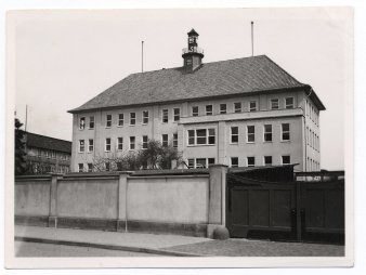 Hausansicht von vorne mit Grundstücksmauer und Einfahrtstor im VordergrundSchwarz-Weiß-Fotografie