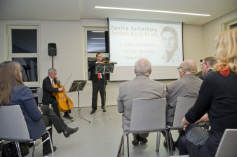 Farbfoto, ein Mann sitzend spielt großes Streichinstrument, ein Mann stehend spielt kleines Streichinstrument