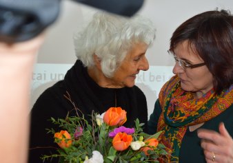 Farbfoto, zwei Frauen einander zuwendend mit Blumenstrauß