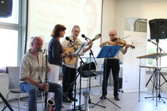 Drei Männer und eine Frau stehen auf einer Bühne und musizieren. Die Frau singt.