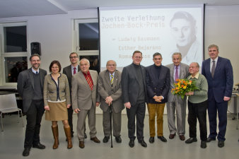 große Personengruppe vor einer Leinwand mit großformatigem Bild eines jungen Mannes