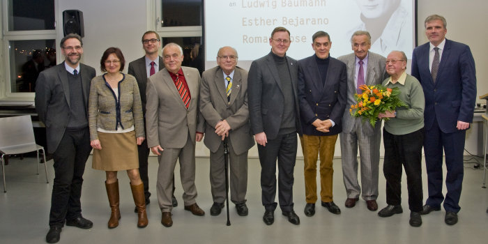 große Personengruppe vor einer Leinwand mit großformatigem Bild eines jungen Mannes