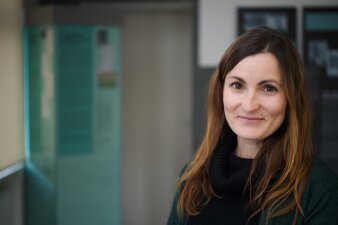 Eine Frau mit langen brauchen Haaren und braunen Augen lächelt in die Kamera.