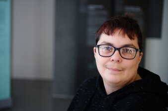 Eine Frau mit kurzen roten Haaren und einer schwarzen Brille lächelt in die Kamera.