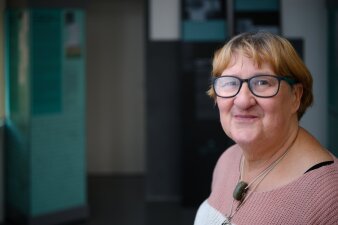 Eine blonde Frau mit kurzen Haaren, Brille und rosa-weißem Strickpullover lächelt in die Kamera.