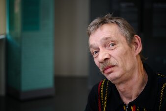 Ein Mann mit Stickpullover und einem Schnurbart schaut seitlich in die Kamera.