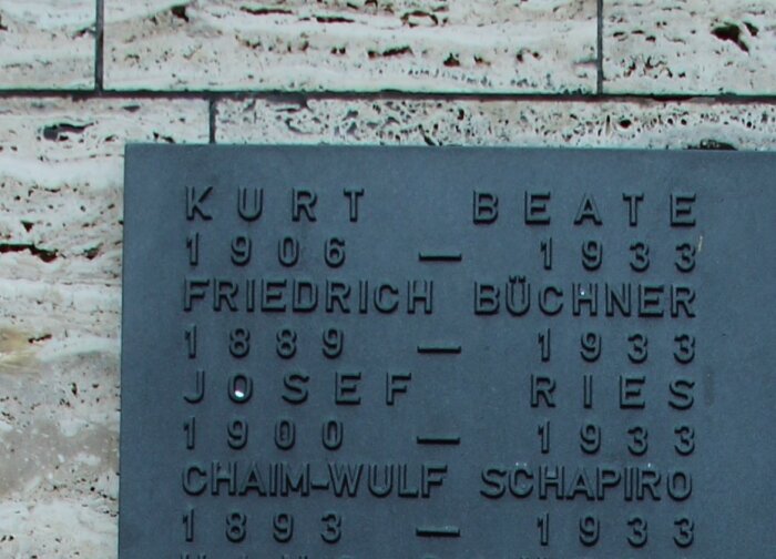 Metalltafel mit Namen und Lebensdaten auf einer Steinmauer