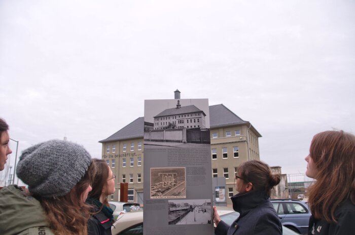 Außenausstellung des Erinnerungsortes Topf & Söhne Eine Gruppe schaut auf eine Informationsstehle. Im Hintergrund das Gebäude des Erinnerungsortes Topf & Söhne.
