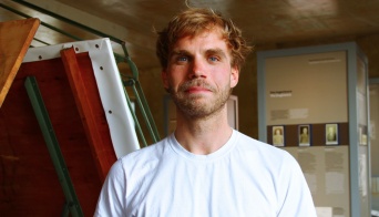 Julian Kusebauch Ein Mann in einem weißen Oberteil in einer Ausstellung.
