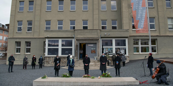 Fünf Menschen halten inne vor einer Steinplatte im Gedenken an Opfer des Nationalsozialismus.